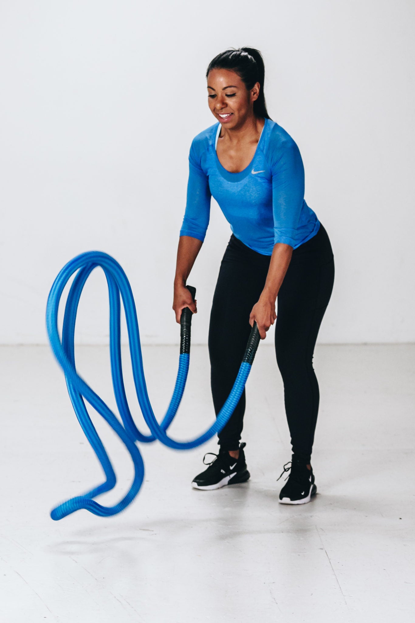 Image of female model doing battle rope waves exercise with unanchored blue hyper rope that is floating off the ground