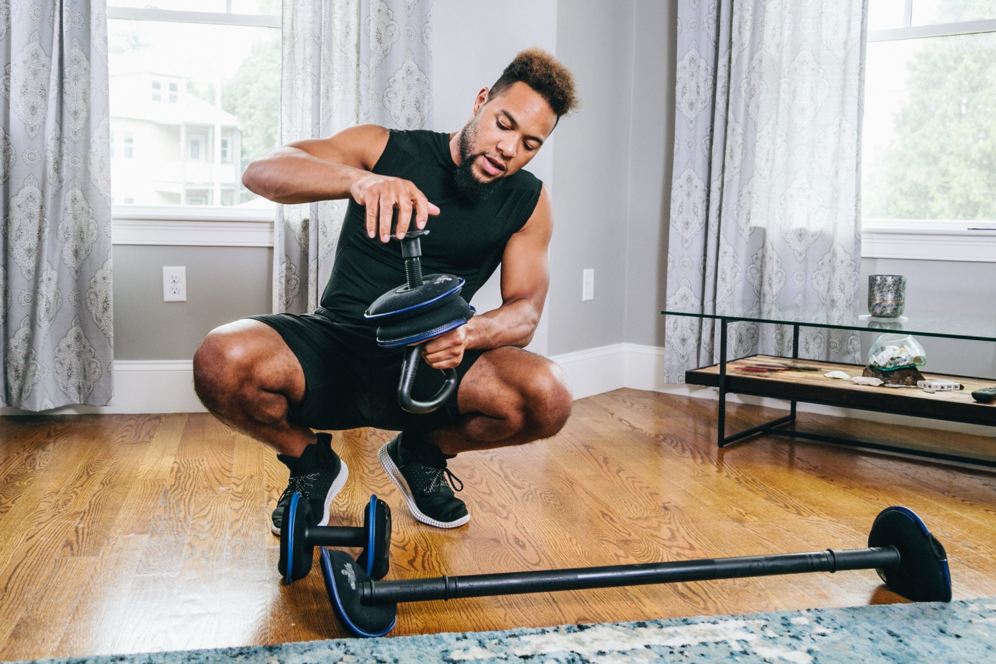 Image of a person at home in a room with a wood floor with Hyperwear SoftBell adjustable dumbbell, soft kettlebell, and cardio barbell