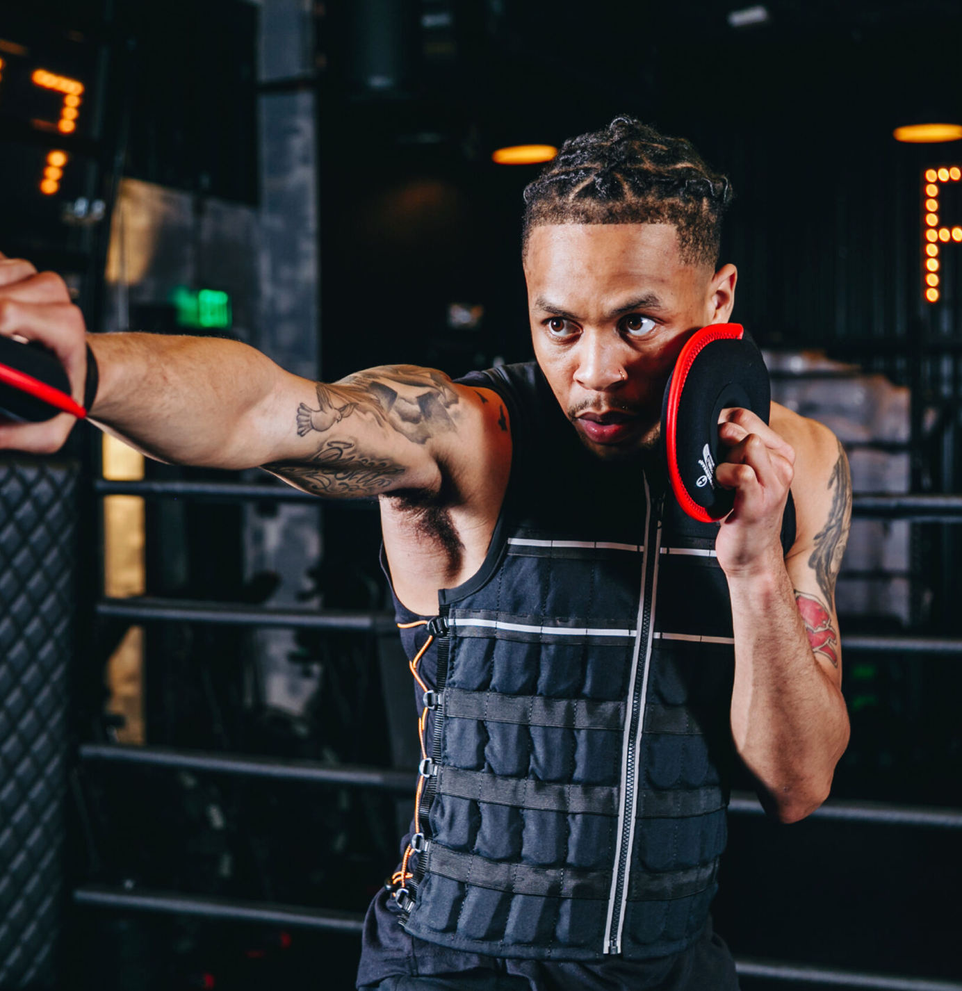picture in a boxing gym of boxer wearing black hyper vest elite weight vest and shadow boxing while holding 2 pound soft neoprene weight plates