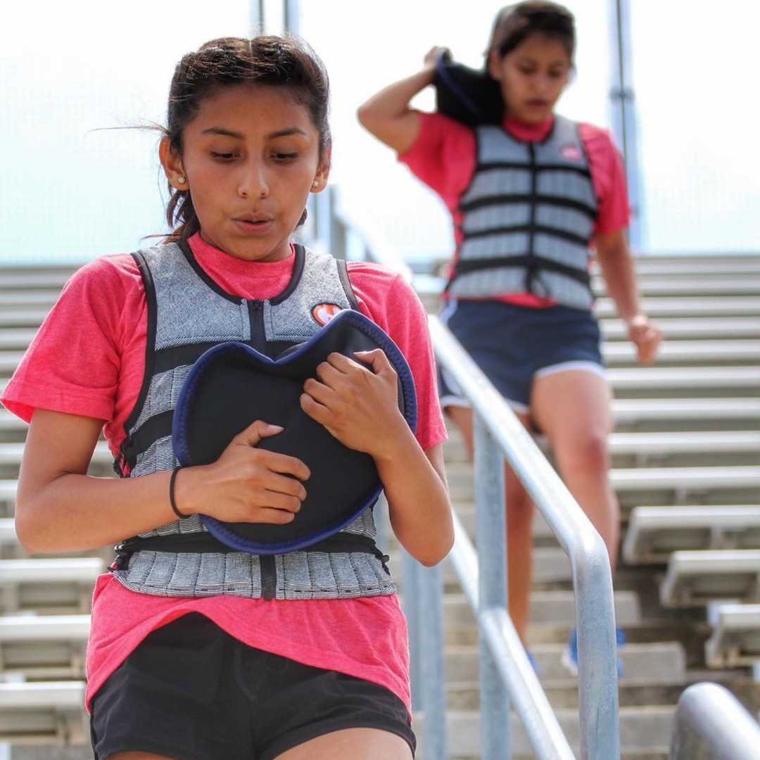 picture of middle school athletes running stadium steps wearing a hyper vest weight vest and carrying a sandbell sandbag