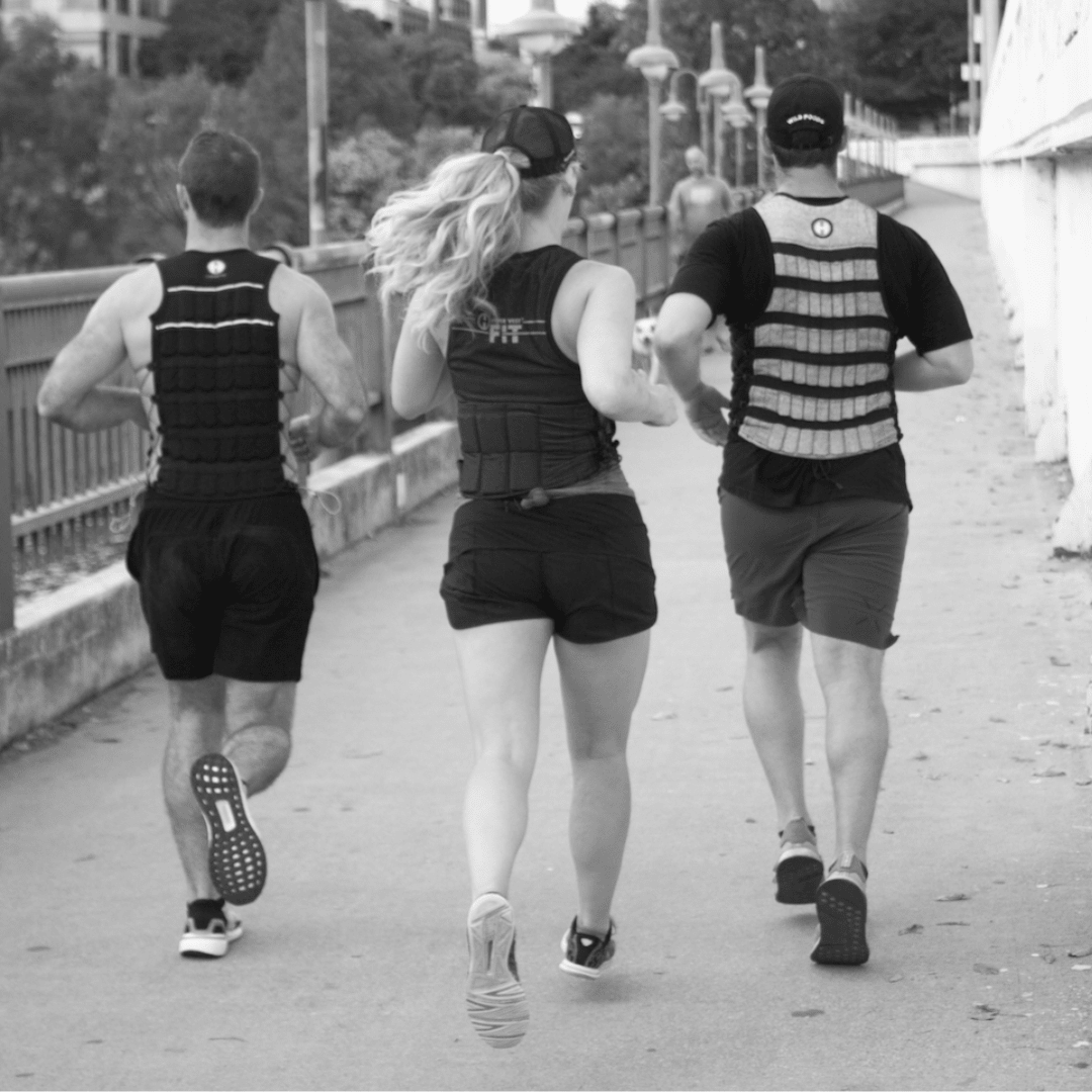 Two walkers wearing Hyperwear weighted vests on a neighborhood path during an autumn walk.