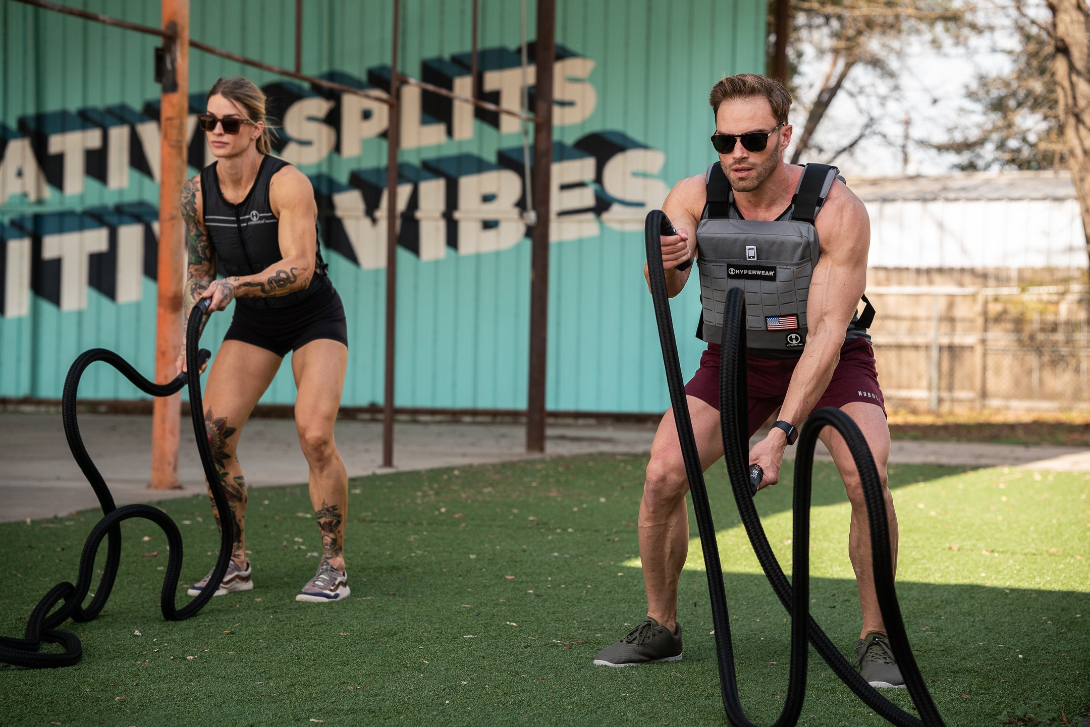 Male and female fitness models are pictured using hyperwear weighted battle ropes and wearing hyper vest weight vests in an outdoor workout session
