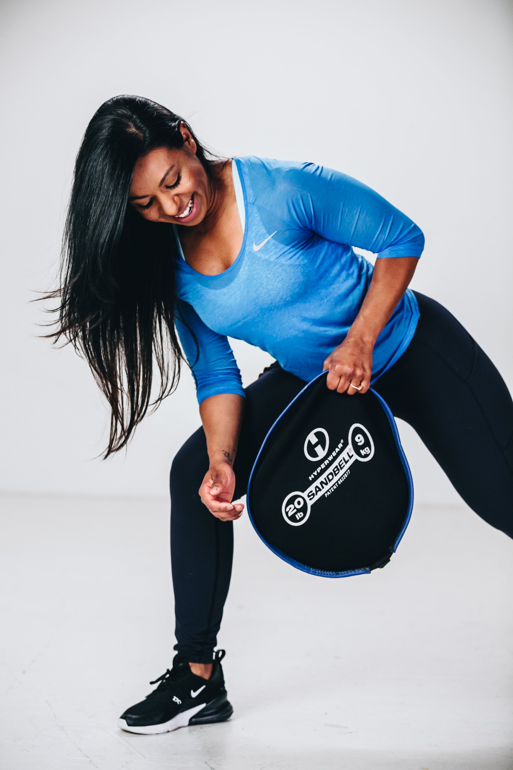 image of female fitness model doing a front lunge gripping a sandbell workout sandbag in one hand