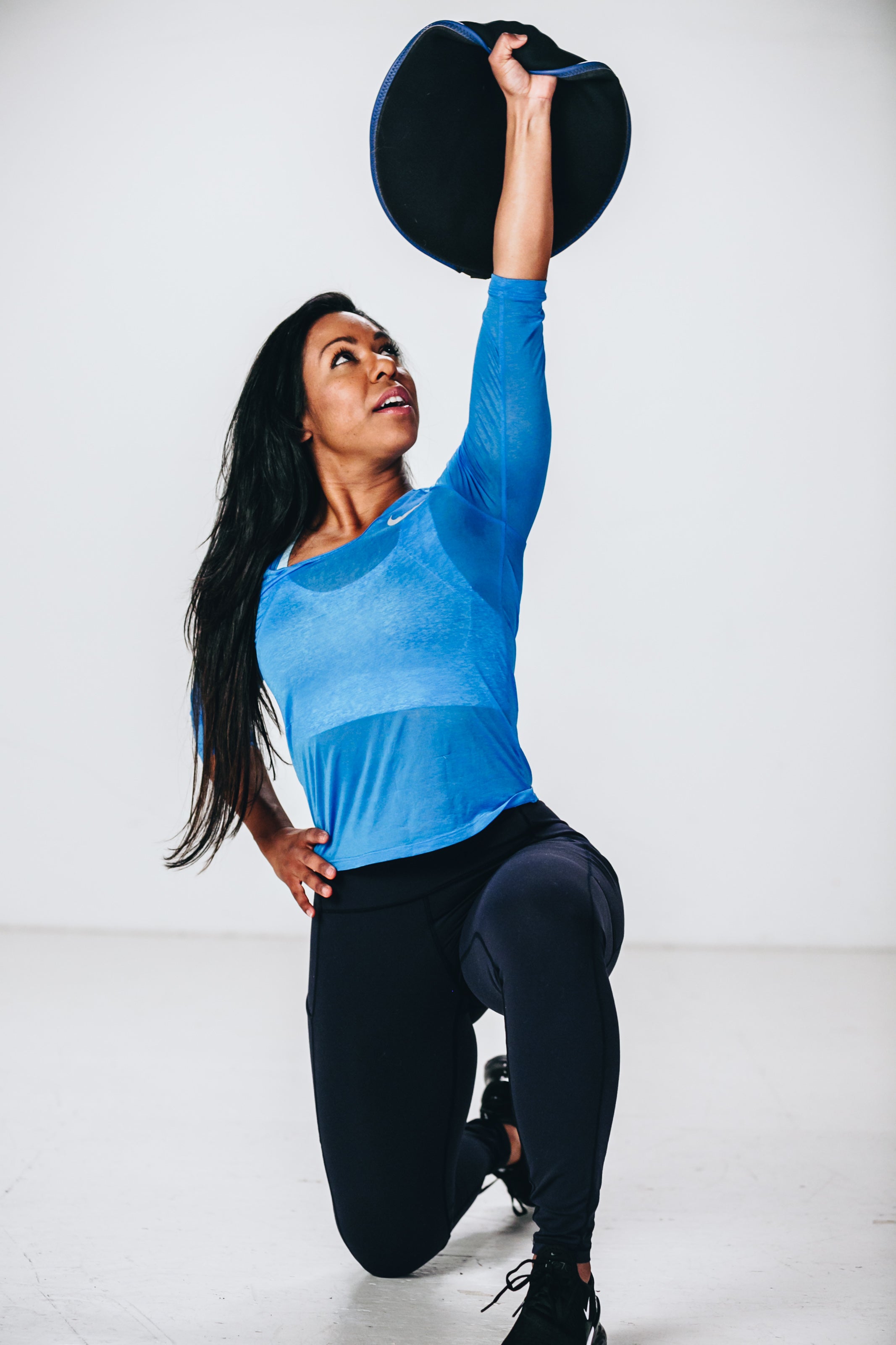 picture of female fitness model executing a lunge while holding sandbell fitness sandbag overhead with arm fully extended