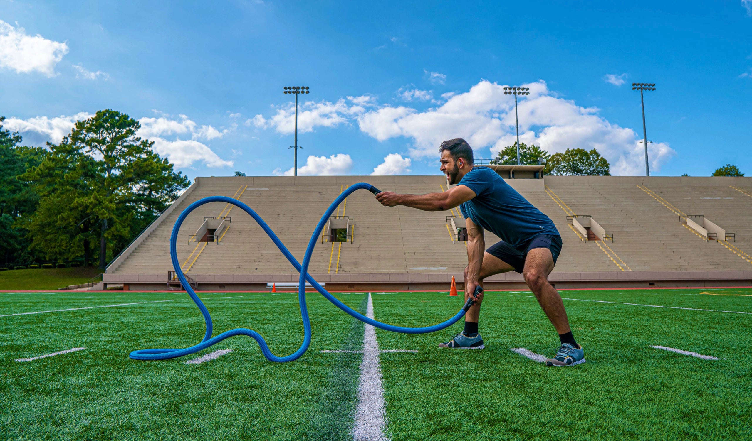 picture of male athlete model on a field in a stadium using a blue hyper rope weighted battle rope to do the wave exercise without any anchor