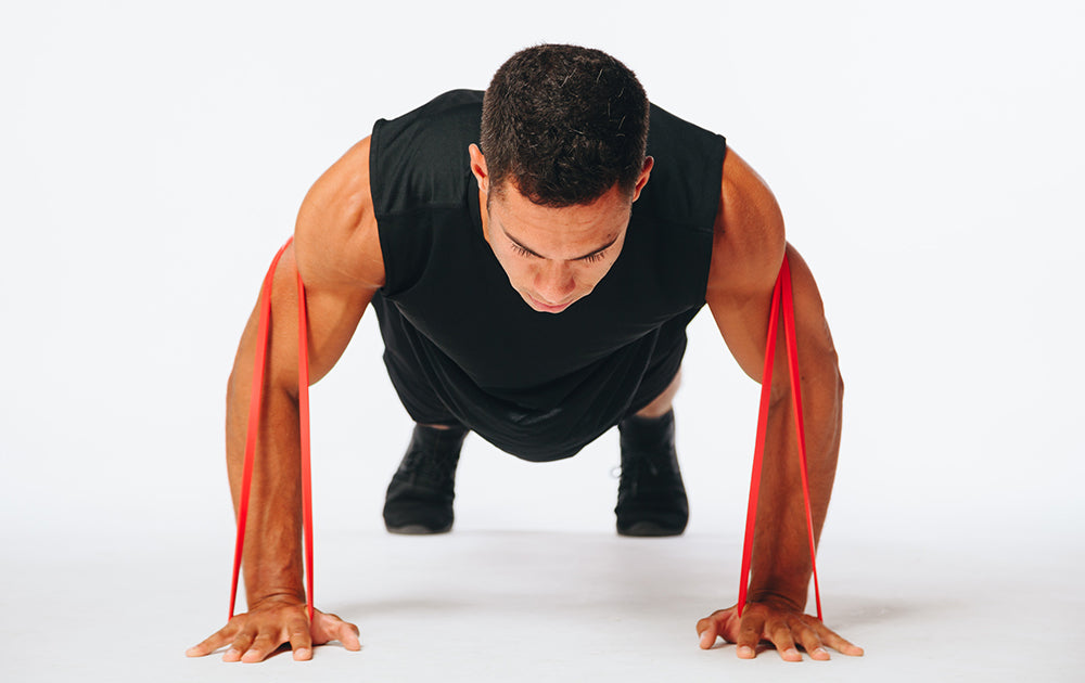 image of a fitness model doing a resisted push up with a super band resistance band over his shoulder