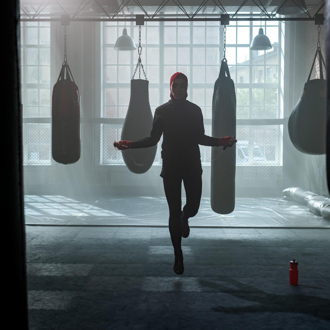 an image of a boxer jumping rope in silhouette indoors with heavy bags and a large window in the background