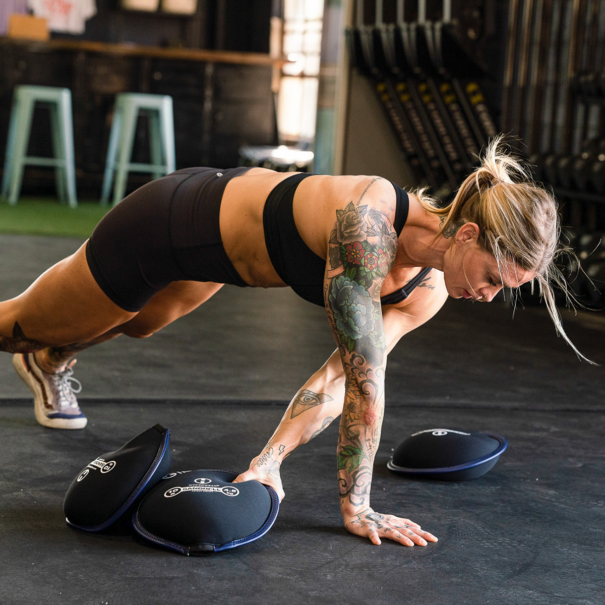 female in a gym setting at crossfit holding a sandbell free weight in prone plank position