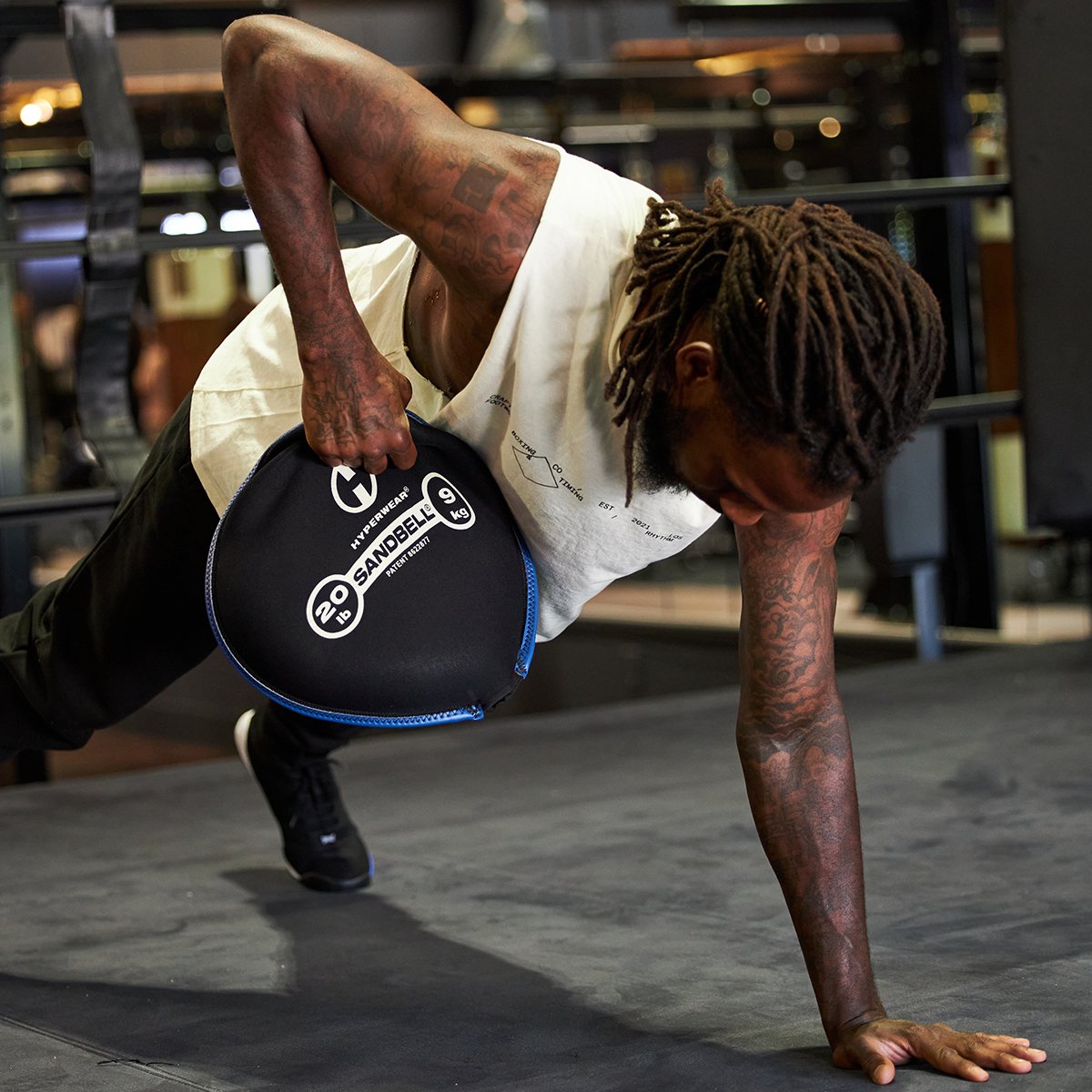 Picture of a male fitness model in a plank position holding a SandBell free weight in one hand